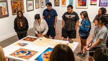Students gather around a table and look at artwork.
