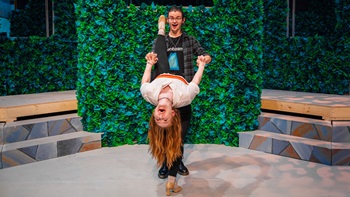 One theatre student leans backwards while holding the hands of another student who is standing.