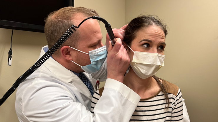 A doctor in a white coat observes a patient's ear.