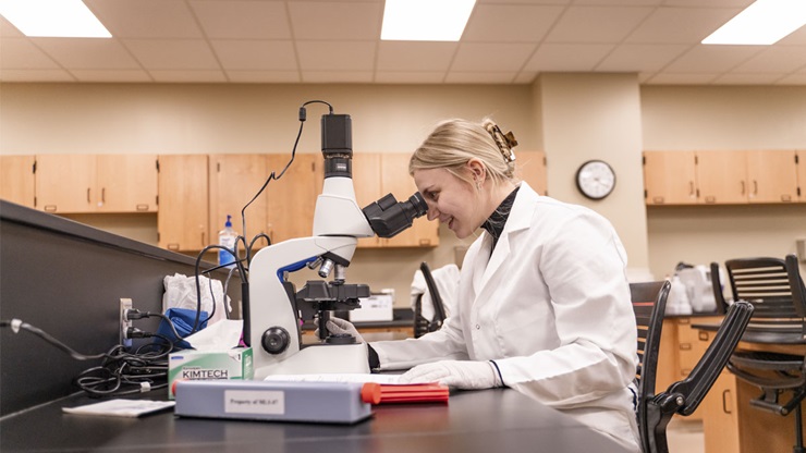 An MLS student is looking through a microscope in the MLS lab at USD