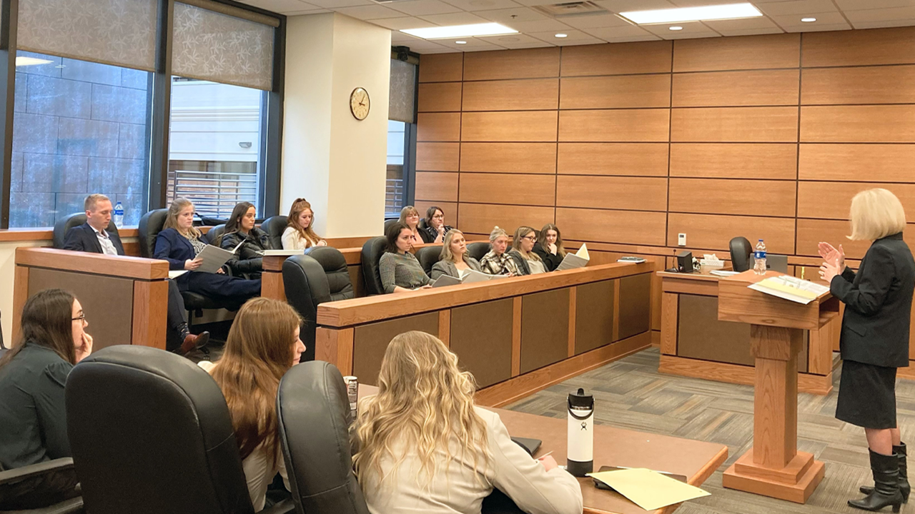 Students sit in a room at a courthouse and learn from a teacher.