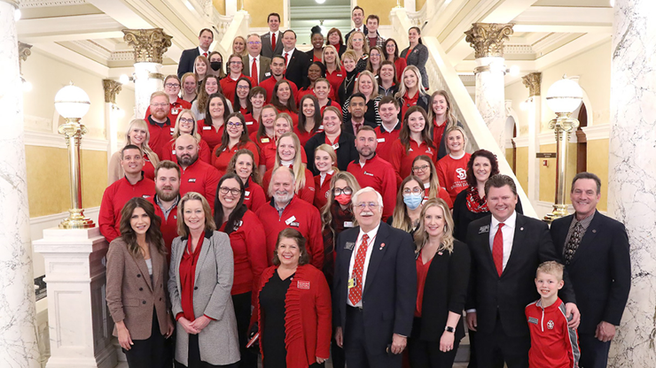 A group photo of USD students, faculty and staff and state employees pose for a photo on stairs in the South Dakota state capitol building.