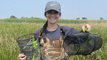Elle Hoops stands in a field of grass and holds up traps to catch amphibians for research.