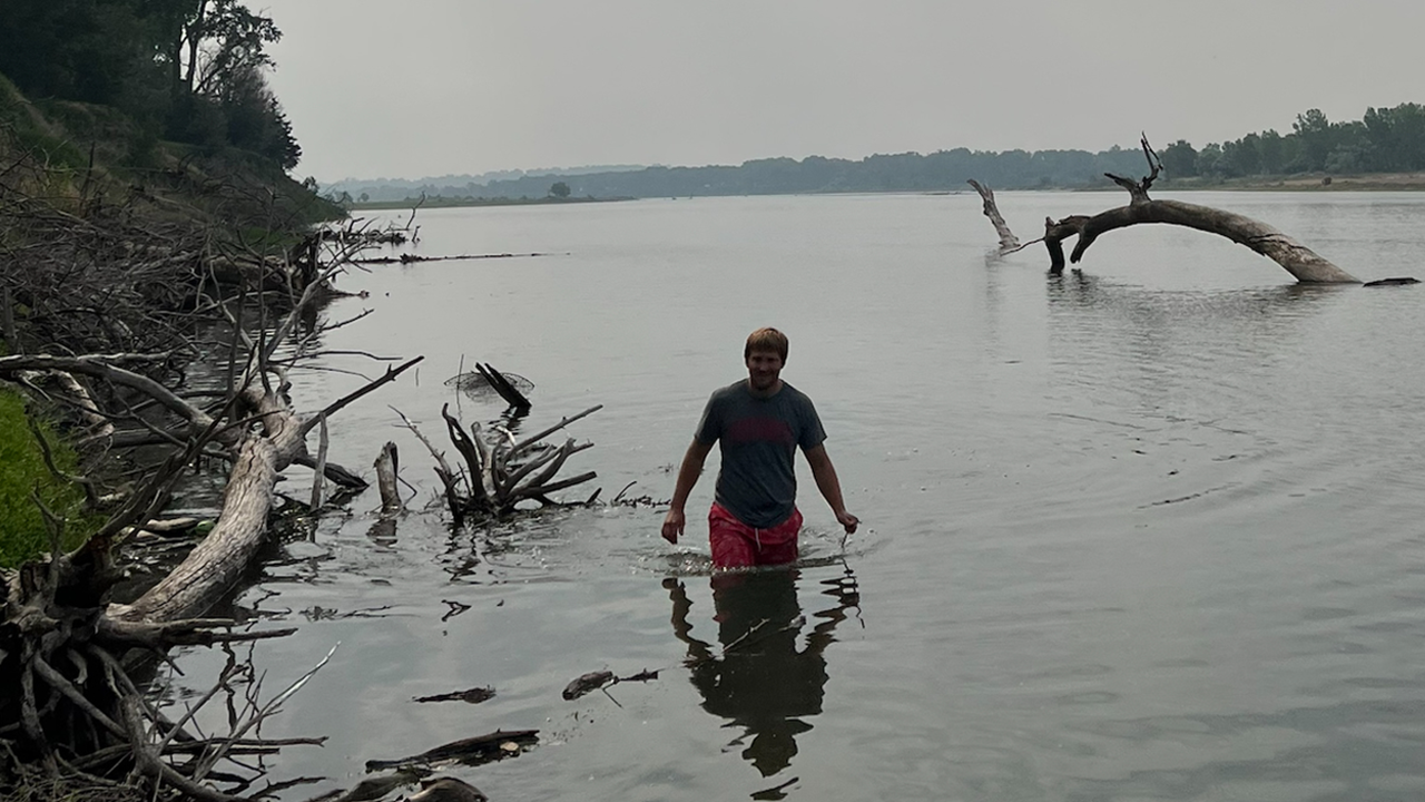 Grant Budden wades through water along the bank of a river.