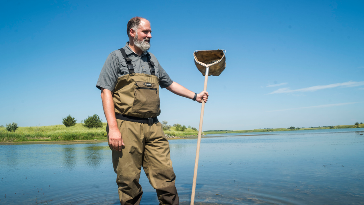 A person wears overalls and holds a net while standing in a large body of water.
