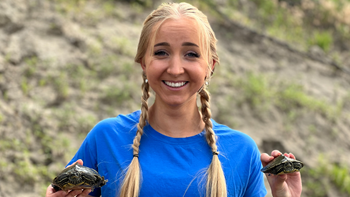 Elizabeth Brust smiles for a picture while holding up two small turtles in her hands.
