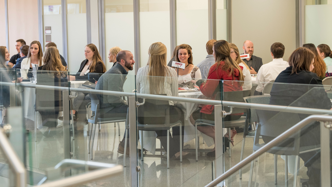 Business students sit at tables and network with businesses at a career fair.