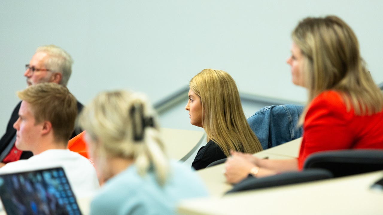 Five audience members sit and look forward towards a presentation.