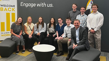 Students in the FMA chapter at USD and their advisor sit on and stand behind a couch and smile for a photo.