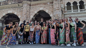 A group of about 20 business students pose for photo in front of a building in Southeast Asia.