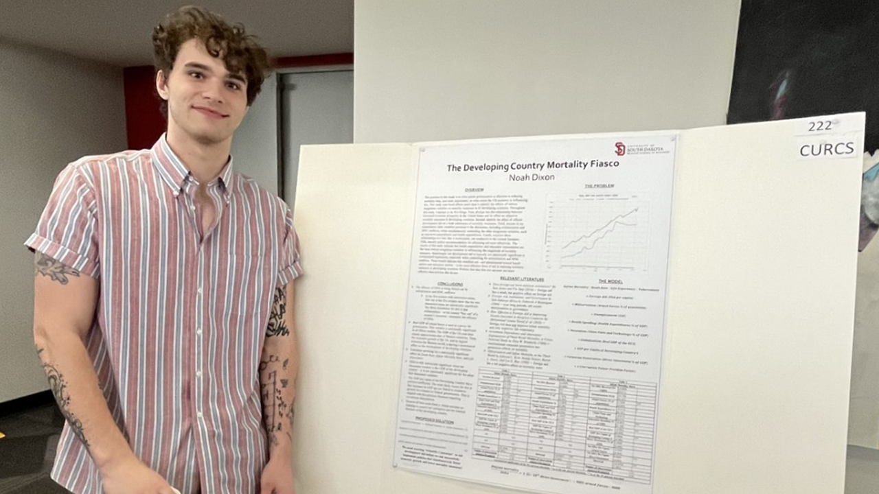 A student stands next to a posterboard to present research findings.