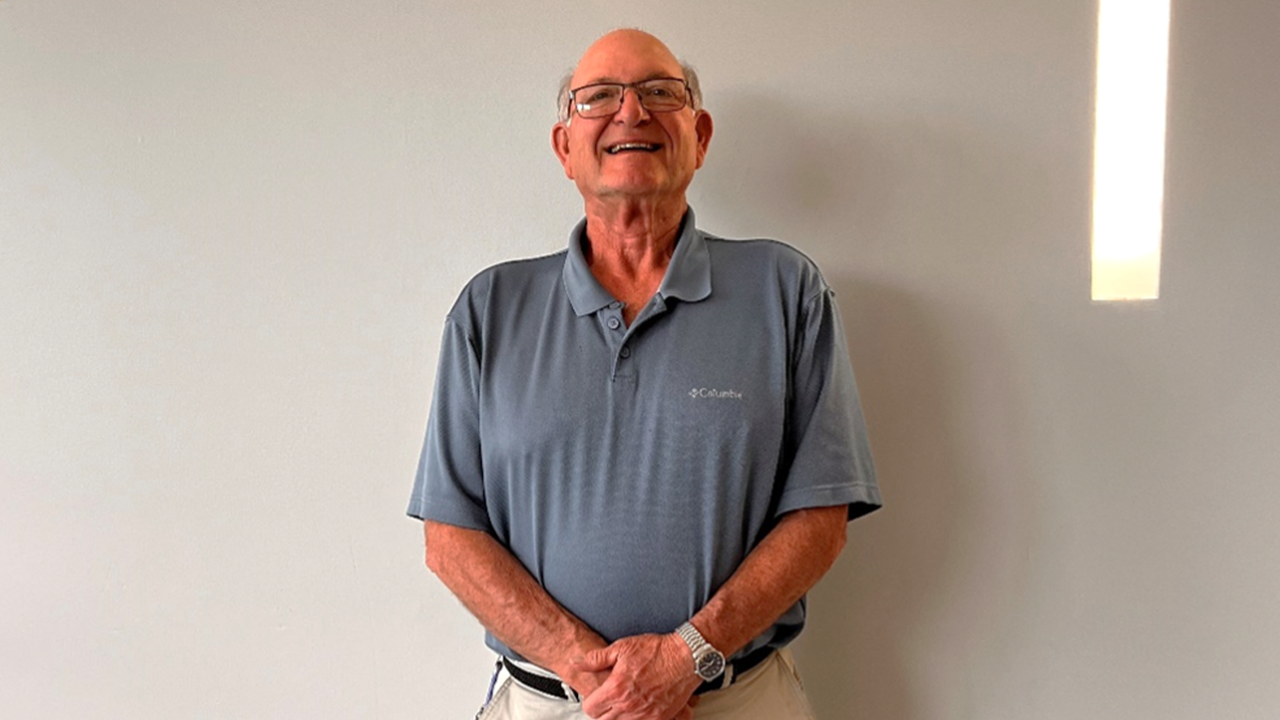 Mitch Morse stands against a wall and smiles with his hands clasped together in front of him.