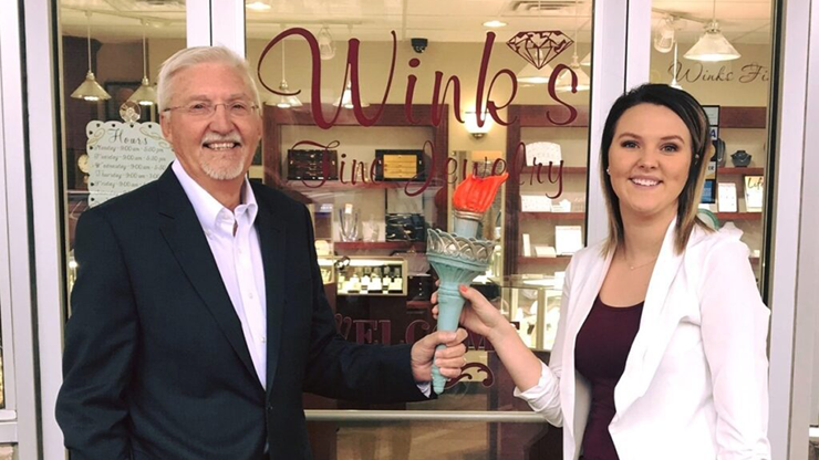 Samantha Tupper and her grandfather stand outside of Wink's Fine Jewelry store and hold a torch.