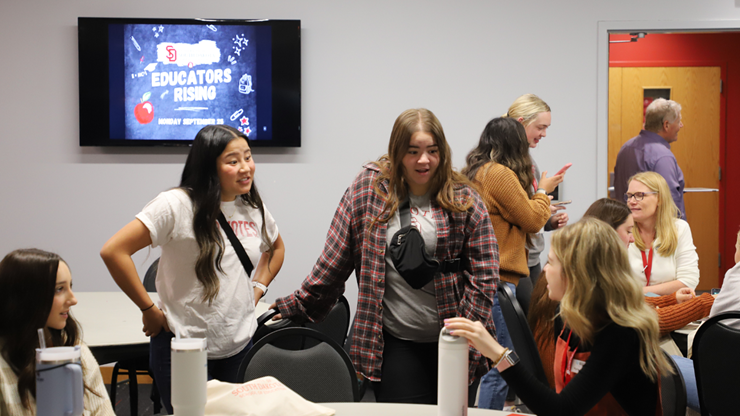 Students talk with one another while sitting and standing around tables.