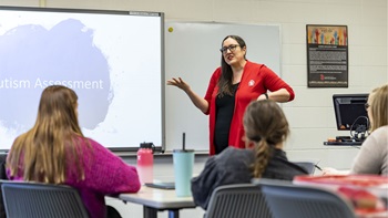 Kari Oyen teaching a class in the school psychology program. She is standing at the front of the classroom, talking with her hands.