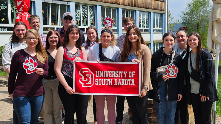 Students hold a University of South Dakota banner in front of a school in Germany.