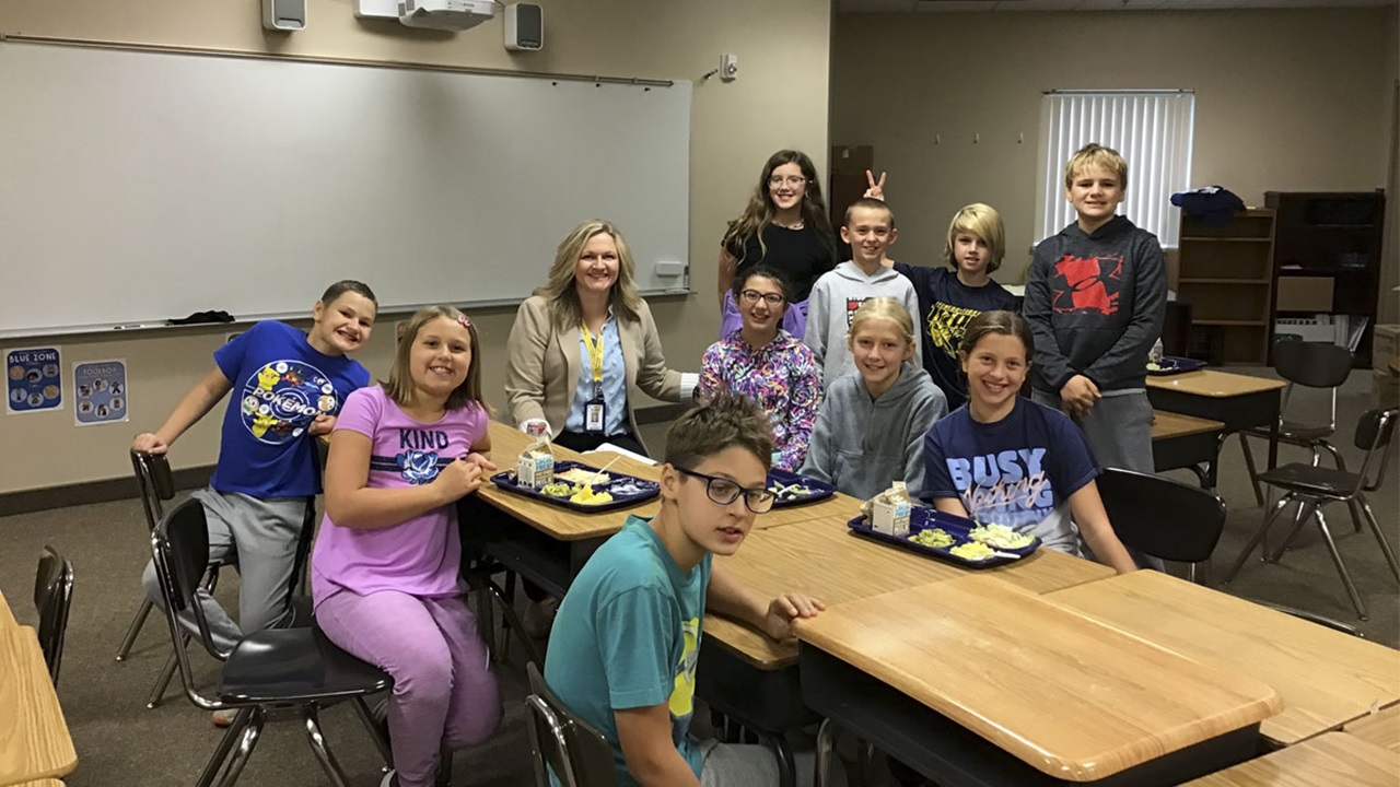 Samantha Walder smiles while sitting at a lunch table with 10 students.