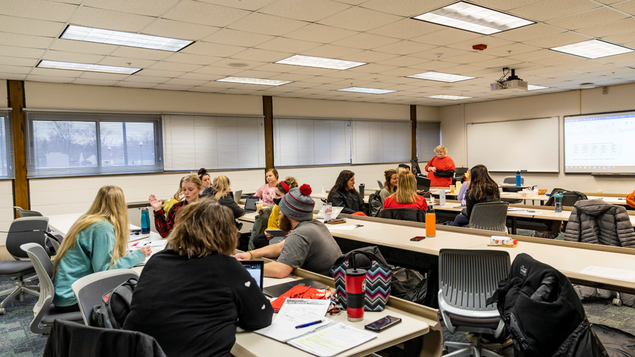 College education students sit at tables in a classroom and learn.
