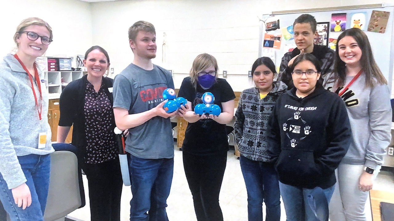 Students stand in a group and hold DASH robots.