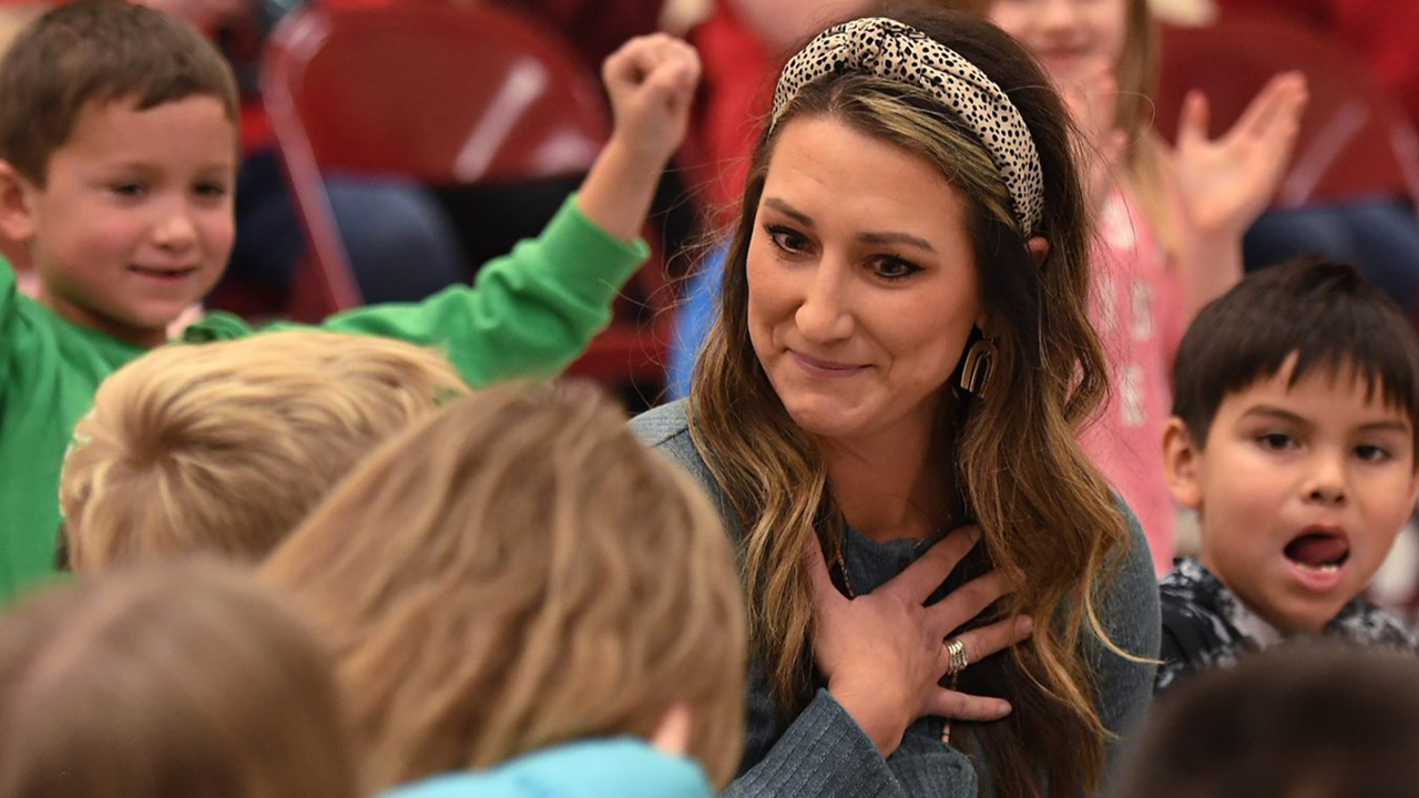 A photo of Abby Turbak with her hand over her heart. She is sitting with her students.