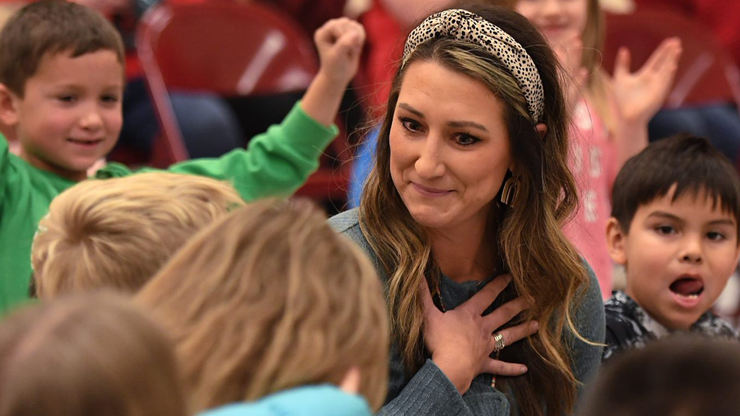 A photo of Abby Turbak with her hand over her heart. She is sitting with her students. 