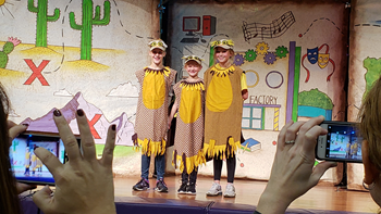 Three young students wearing bird costumes stand on a theatre stage and smile. 