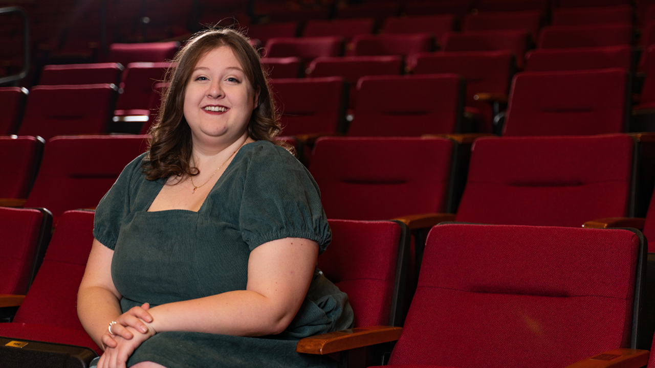 A student sitting in red theatre chairs.