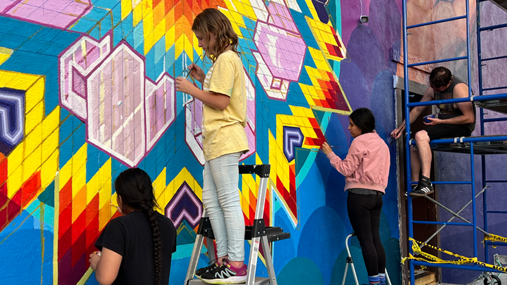 Four school students work together on painting a colorful mural in Vermillion.