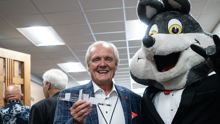 A photo of Scott Lawrence holding up his College of Fine Arts Hall of Fame trophy. He is posing for a photo with Charlie Coyote.
