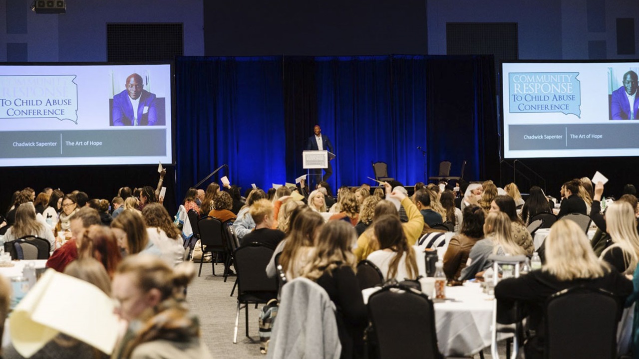 Attendees of the 2022 Community Response to Child Abuse Conference sit at tables listening to presenter Chadwick Sapenter. Attendees of the 2022 Community Response to Child Abuse Conference sit at tables listening to presenter Chadwick Sapenter.
