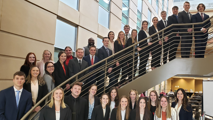 Around 30 physical therapy students dressed in professional attire line up on a set of stairs and in front for a photo.