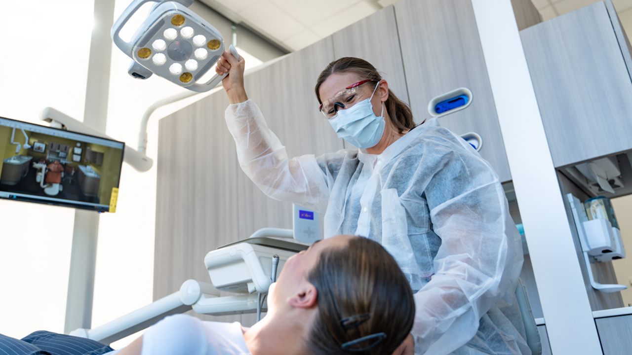 A dental hygienist observes a patient in a dental chair.