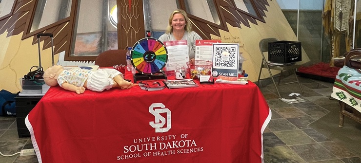 A health sciences recruiter with a stand smiling with various fliers and games.