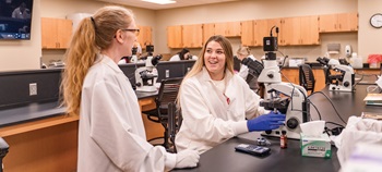 Two medical lab science students smiling and talking in a lab.