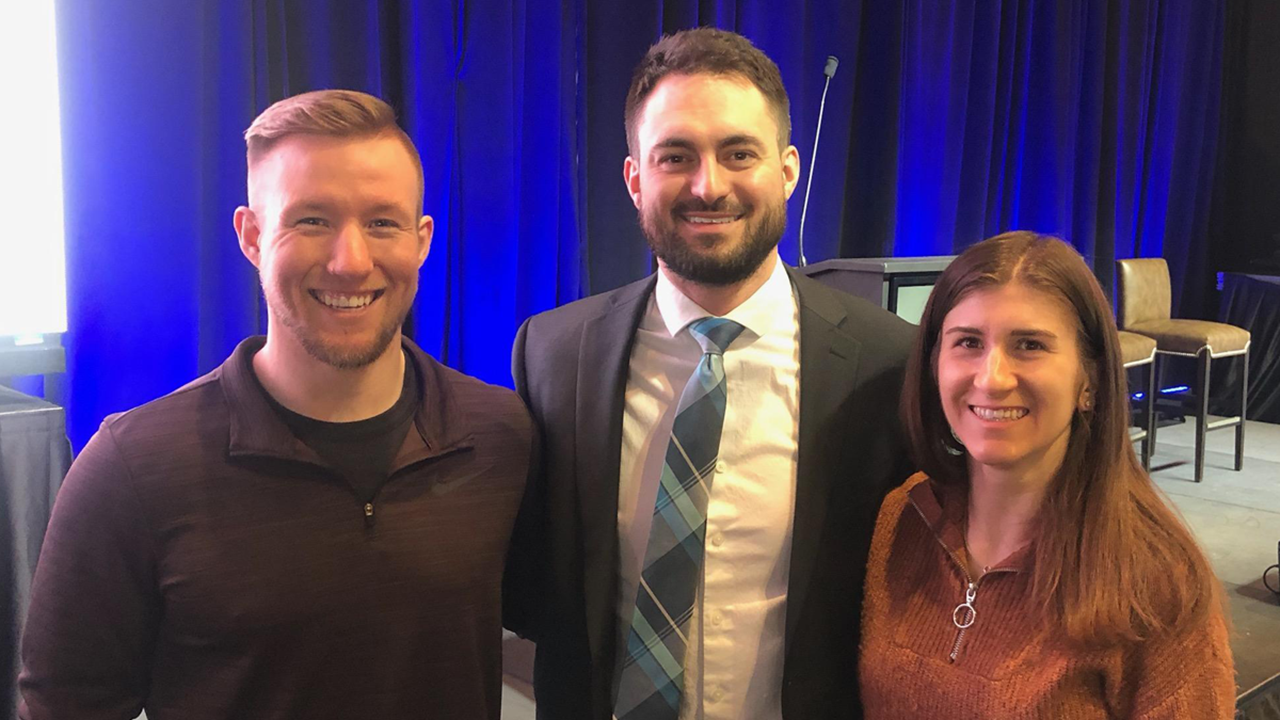 Three physical therapy residents stand side by side with their arms around each other for a photo in front of the stage at the Sanford Sports Medicine Symposium.