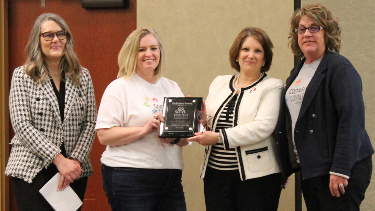 Four people stand together and hold a plaque.