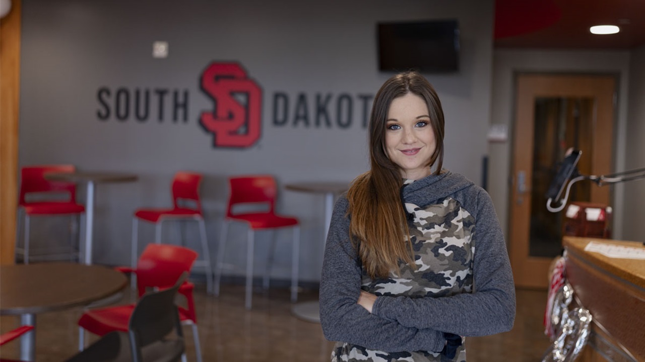 USD - Sioux Falls pre-nursing student Sadi Peck stands in front of a USD sign with her arms crossed. She is smiling at the camera. USD - Sioux Falls pre-nursing student Sadi Peck stands in front of a USD sign with her arms crossed. She is smiling at the camera.