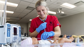 a USD nursing student wears a stethoscope to listen to a mannequin's heartbeat in a simulation