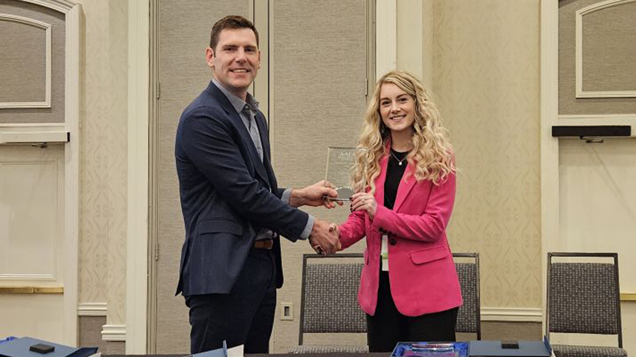 Taylor Bushelle shakes hands with someone while receiving a plaque for her AALA award.