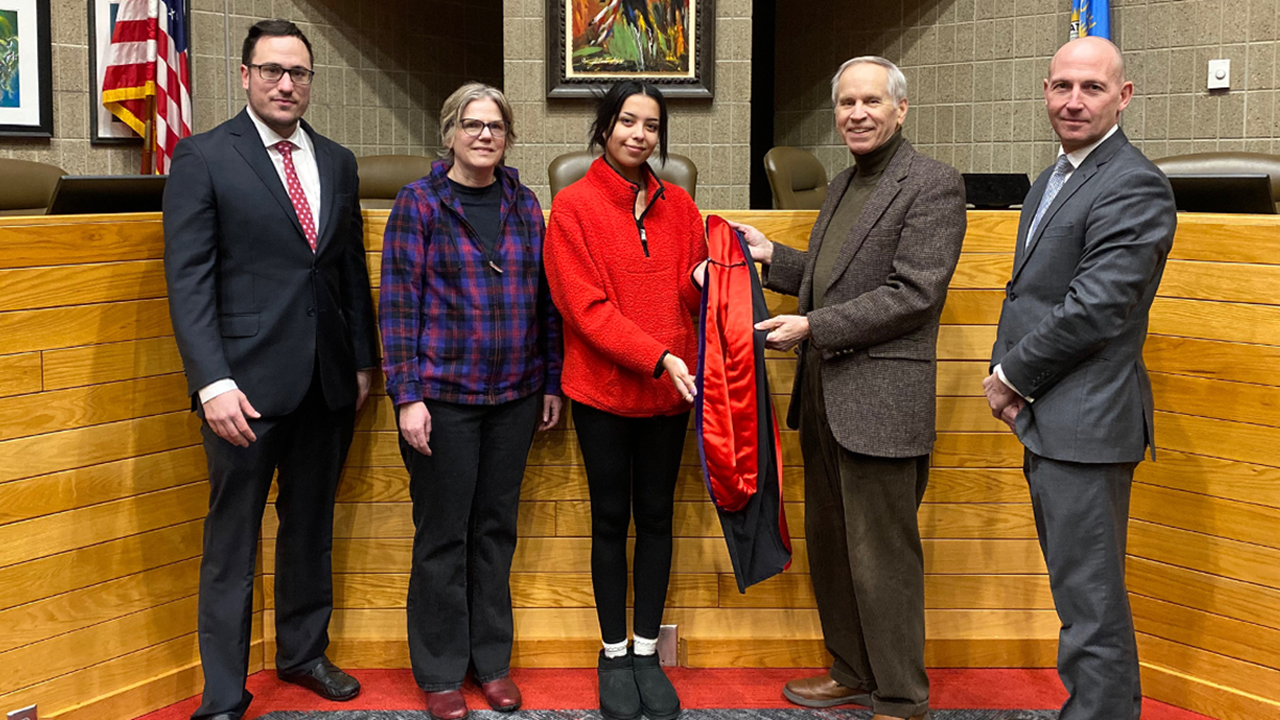 People stand in a law courtroom and hold an academic doctoral hood that was donated to the law school.