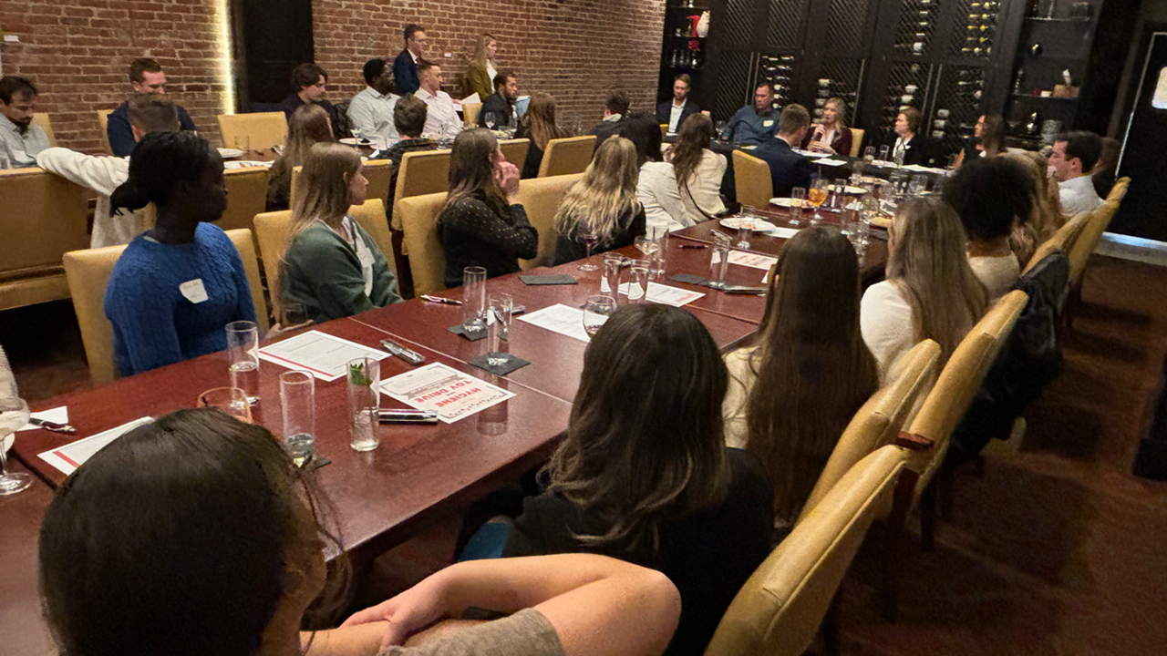 Several medical and legal professionals and students sit along two long tables and listen to a panel of experts.