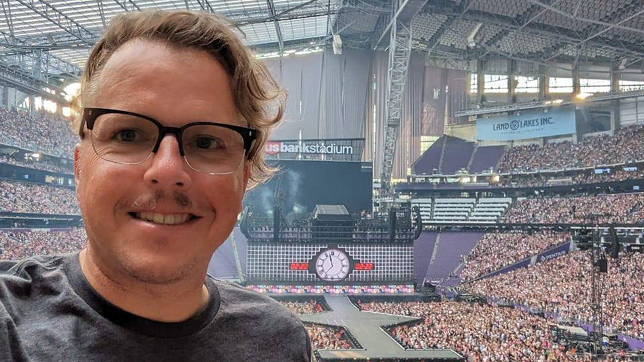 Sean Kammer smiles for a selfie with Taylor Swift's stage behind him and a crowd full of people.