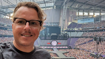 Sean Kammer smiles for a selfie with Taylor Swift's stage behind him and a crowd full of people.