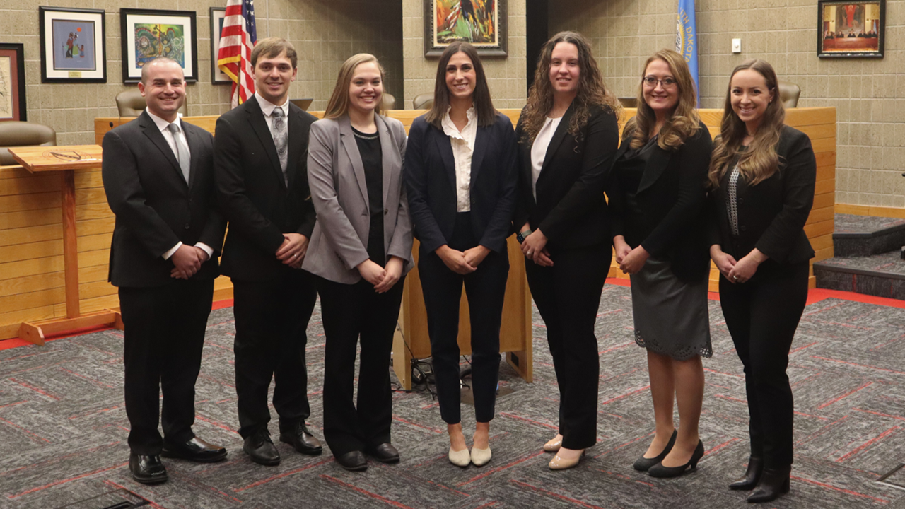 Seven law students who serve as editors for the South Dakota Law Review wear professional attire and stand side by side for a photo in the Knudson School of Law courtroom.