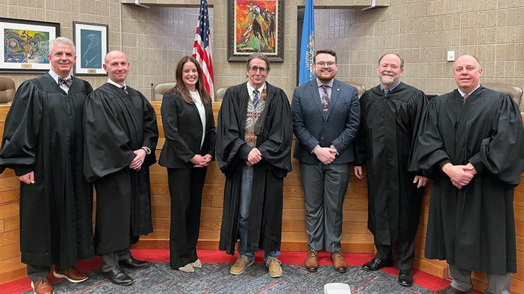 Law students stand with legal professionals wearing robes in a courtroom.