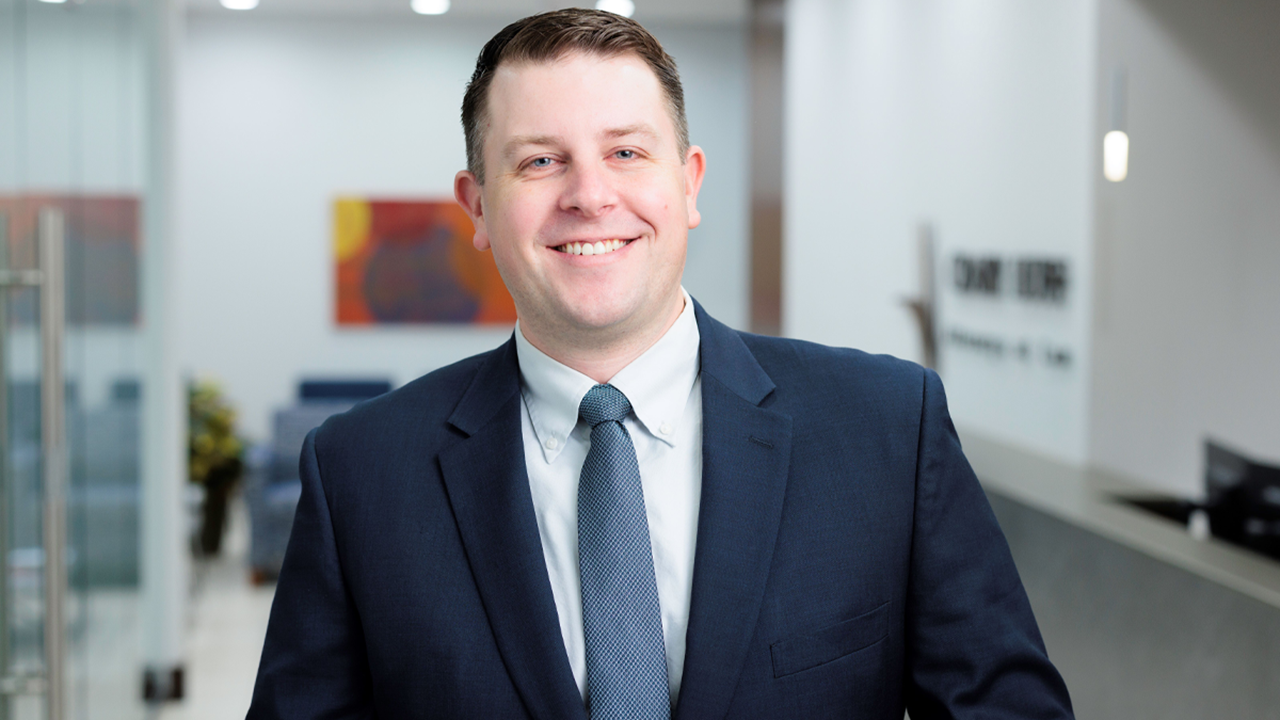 A professional headshot of Matt Gaul. He is wearing a suit, smiling and standing in an office.