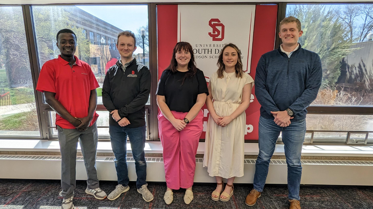 Five law students stand side by side for a photo. They are standing in front of a window.