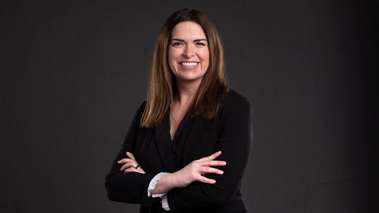 Jessica Messersmith wears a black suit coat and stands against a dark gray background with her arms crossed.