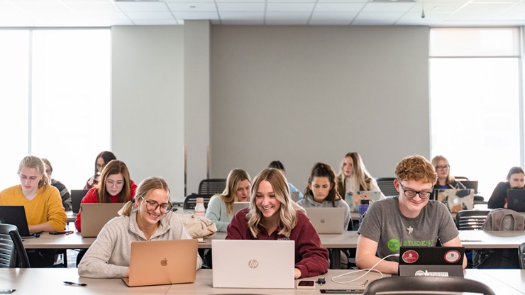 Students sitting at table with computers in classroom