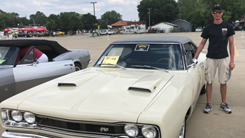 A persons stands next to a tan-colored classic car. 